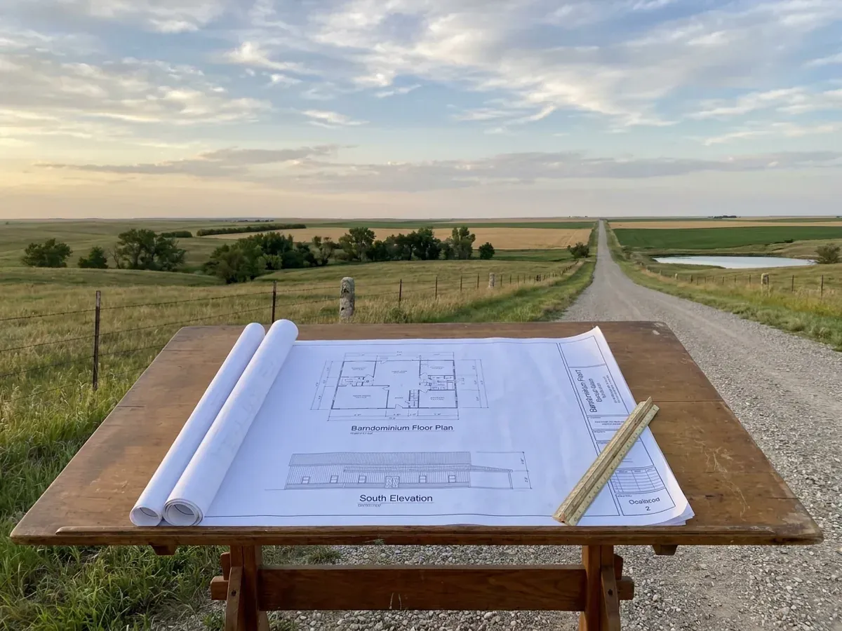 Barndominium floor plan and elevation drawings laid out on a drafting table with a scale rule.